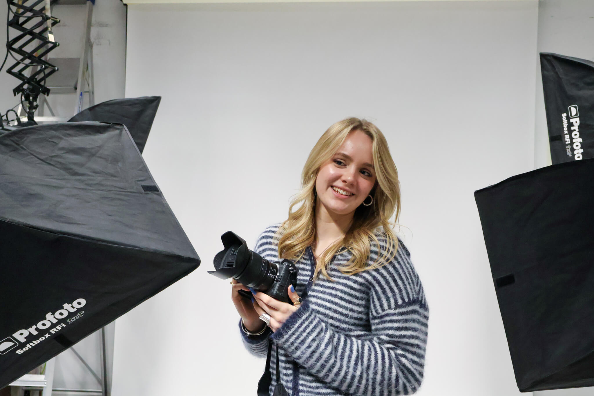 A female fashion photography student in a studio, holding a camera.