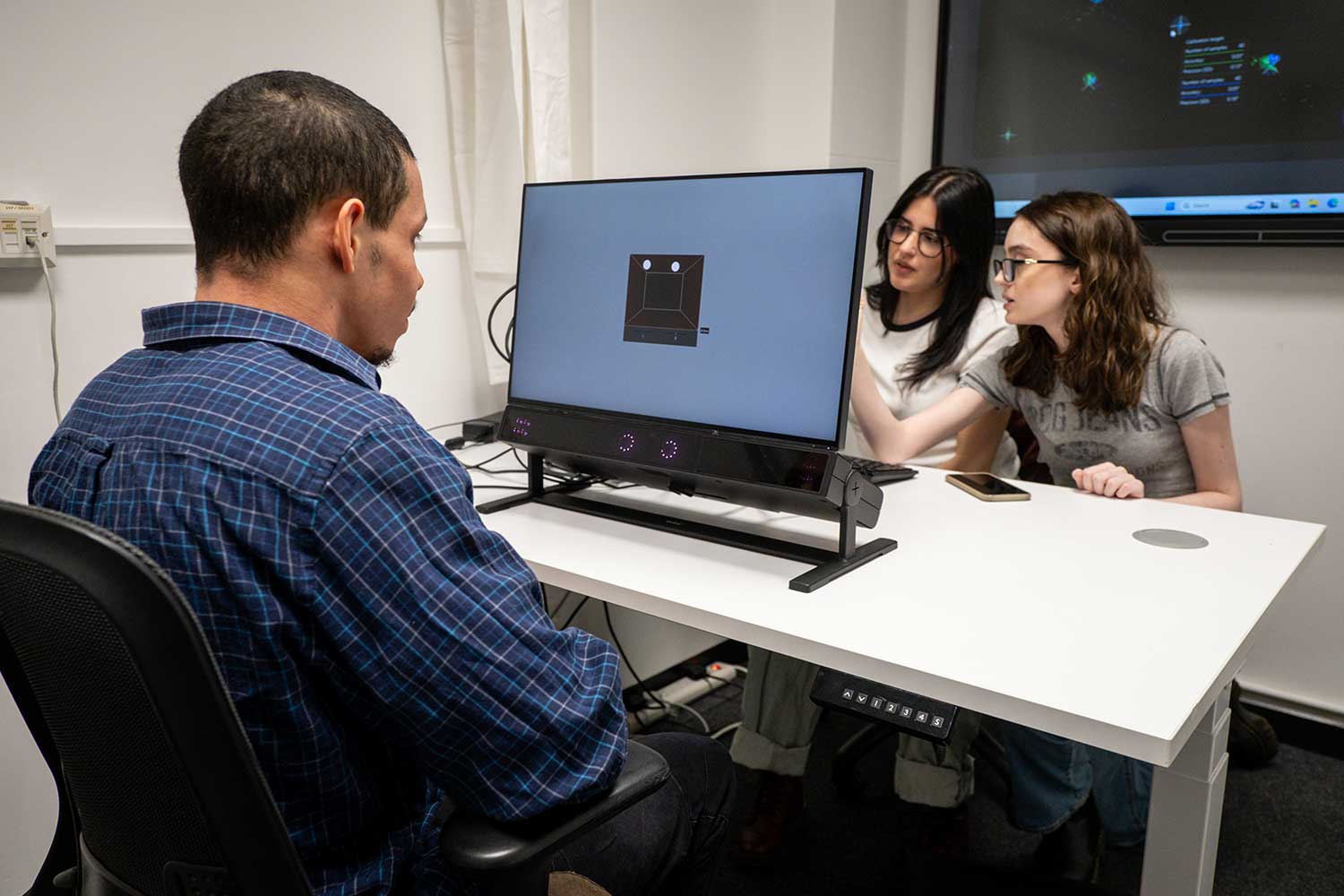 Three students use an eye-tracking device and a computer monitor