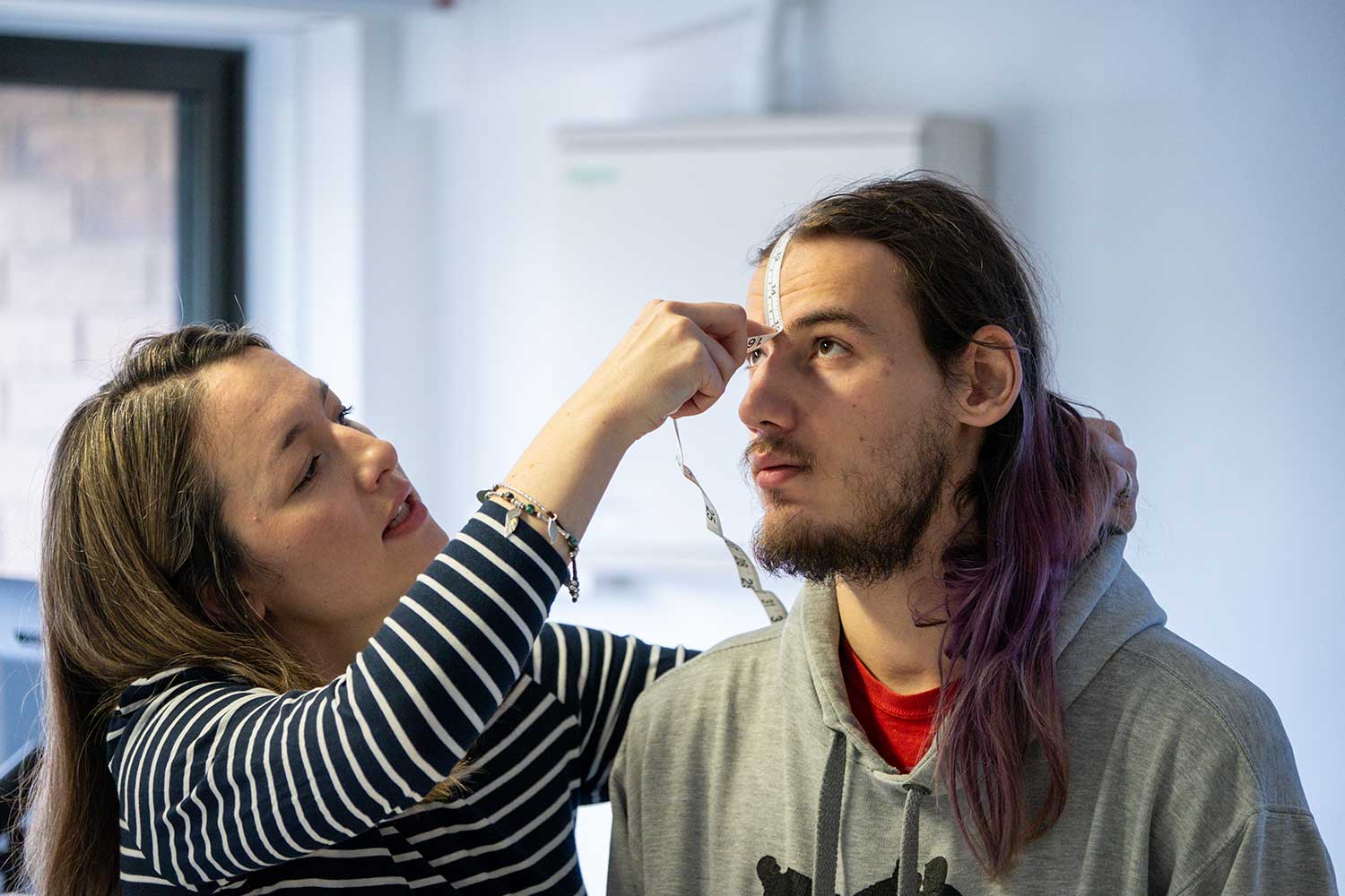 A lecturer measures a student's head with a tape measure