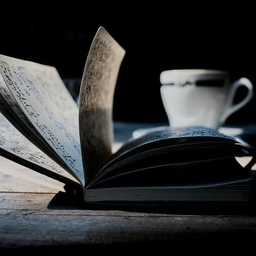 Open book on a table with a mug in the background.