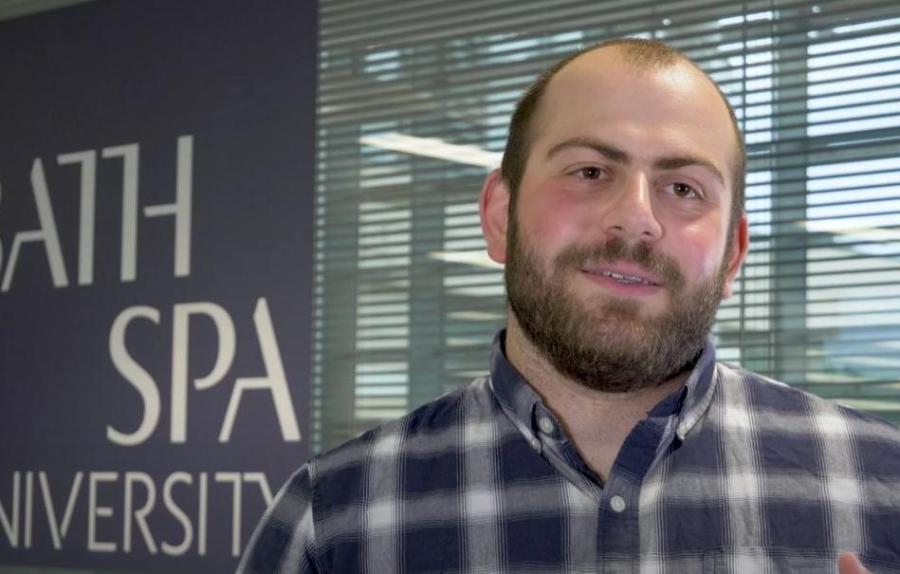 A student wearing a checked shirt talks to the camera