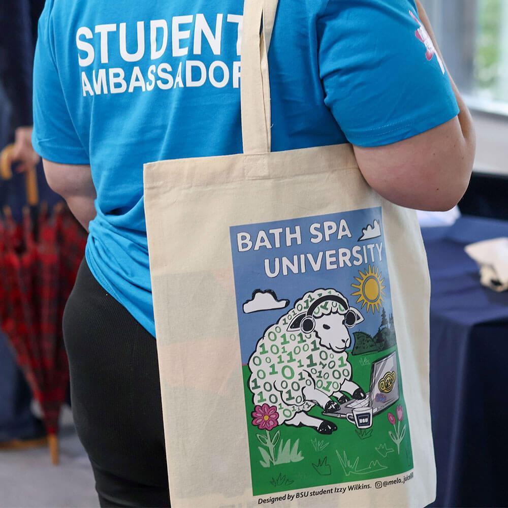 A student ambassador in a blue shirt holds a tote bag with a sheep print