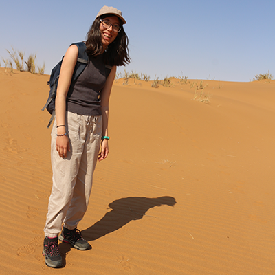 A person with long dark hair stands in a desert