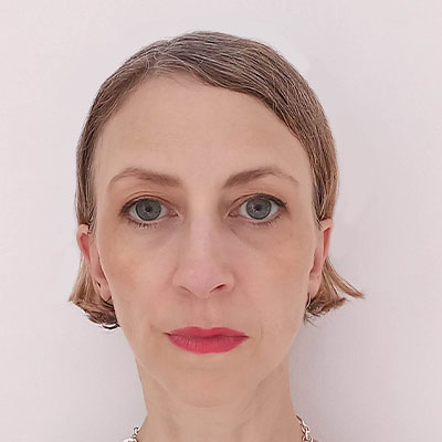 Headshot of person with light brown bob, metallic necklace and white top.