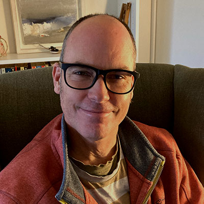 Man wearing glasses, smiling as he looks at the camera
