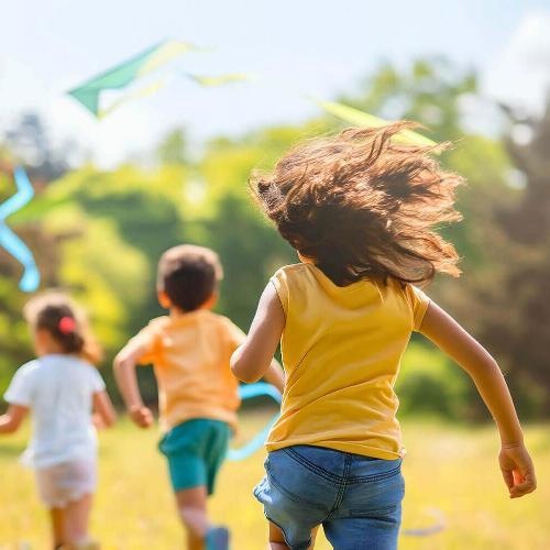 three children run through field towards trees in the distance.